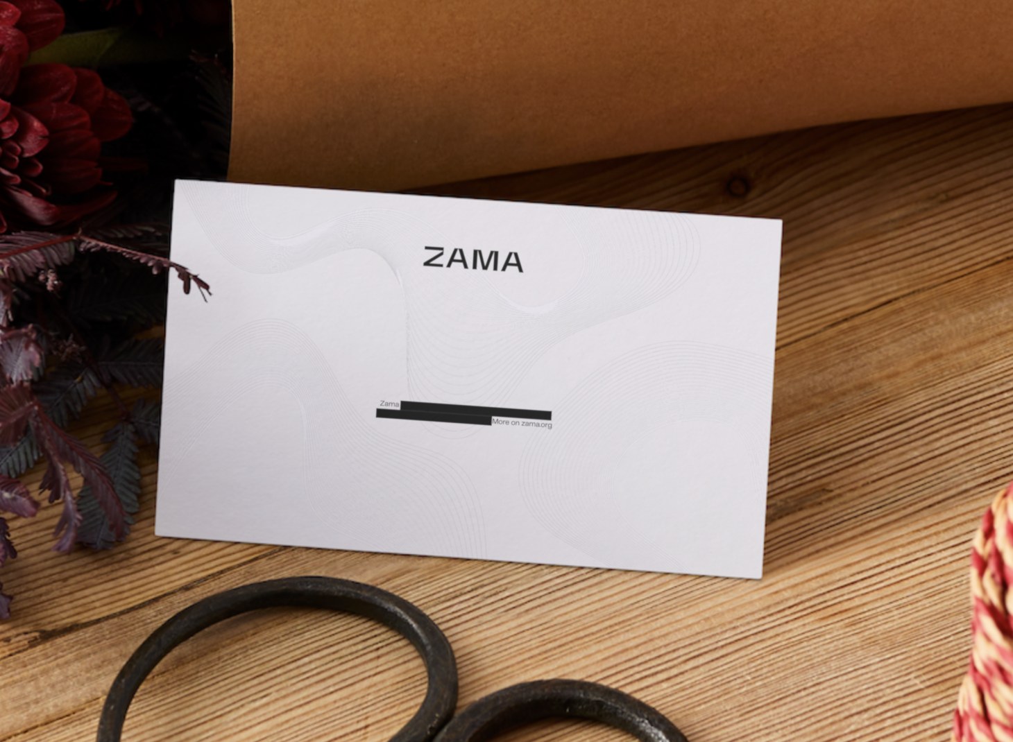 La carte ZAMA posée sur bois, gaufrage de courbes en creux et ligne de texte caviardée